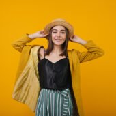 Laughing winsome woman in straw hat posing in studio. Attractive lady in black tank-top isolated on bright orange background.